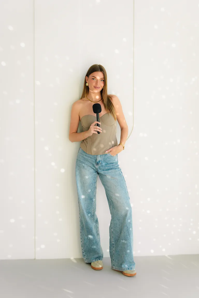 Eline als video host met microfoon tegen een witte wand